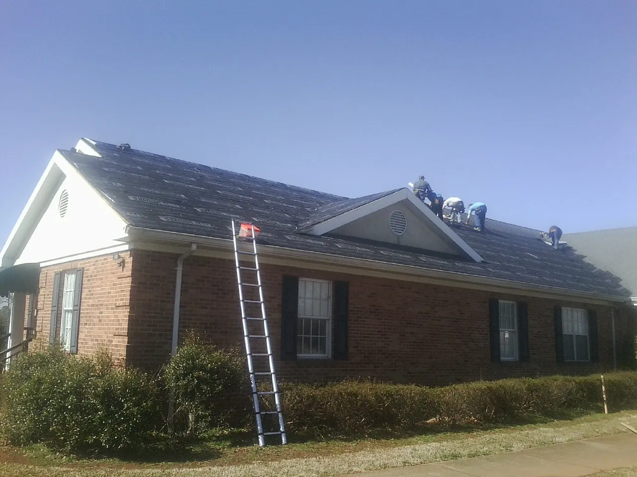 Crew tearing shingles off a brick ranch roof with a ladder set — Metal Roof Repair work by our crew in Savage