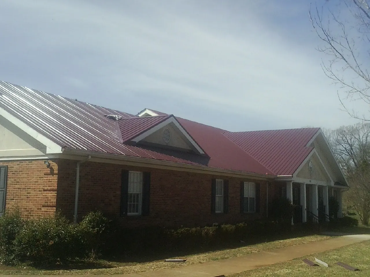 Red metal roof with gabled entries on a long brick building, from a Hail Damage Roof Repair job in Savage