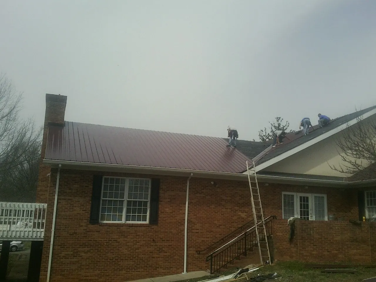 Crew setting red metal roofing panels on a brick home in Savage