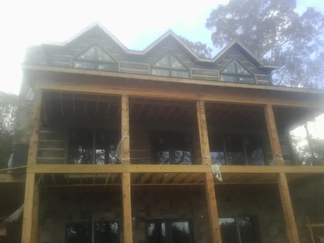Dormers and porch framing on a large log home under construction — Roof Coating work by our crew in Savage