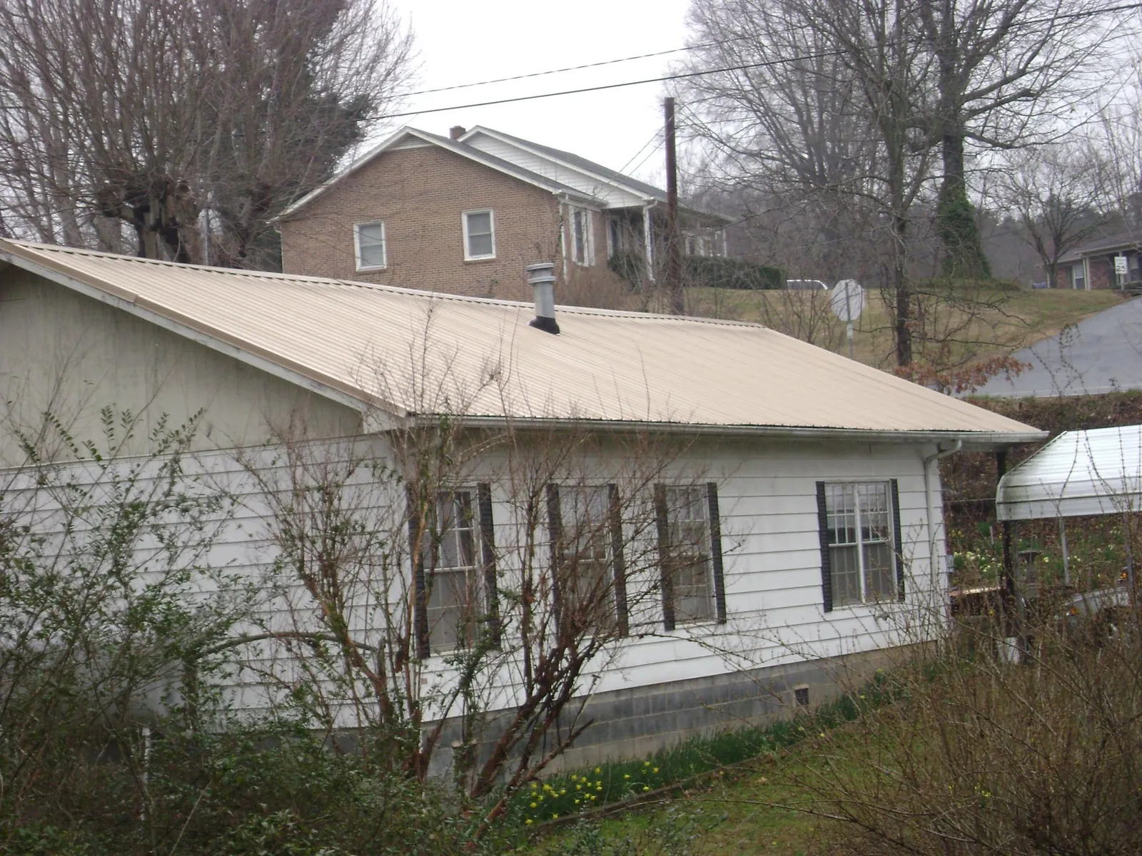Tan metal roof on a white sided house set into a hillside — Commercial Roofing by Roofing Brothers in Savage