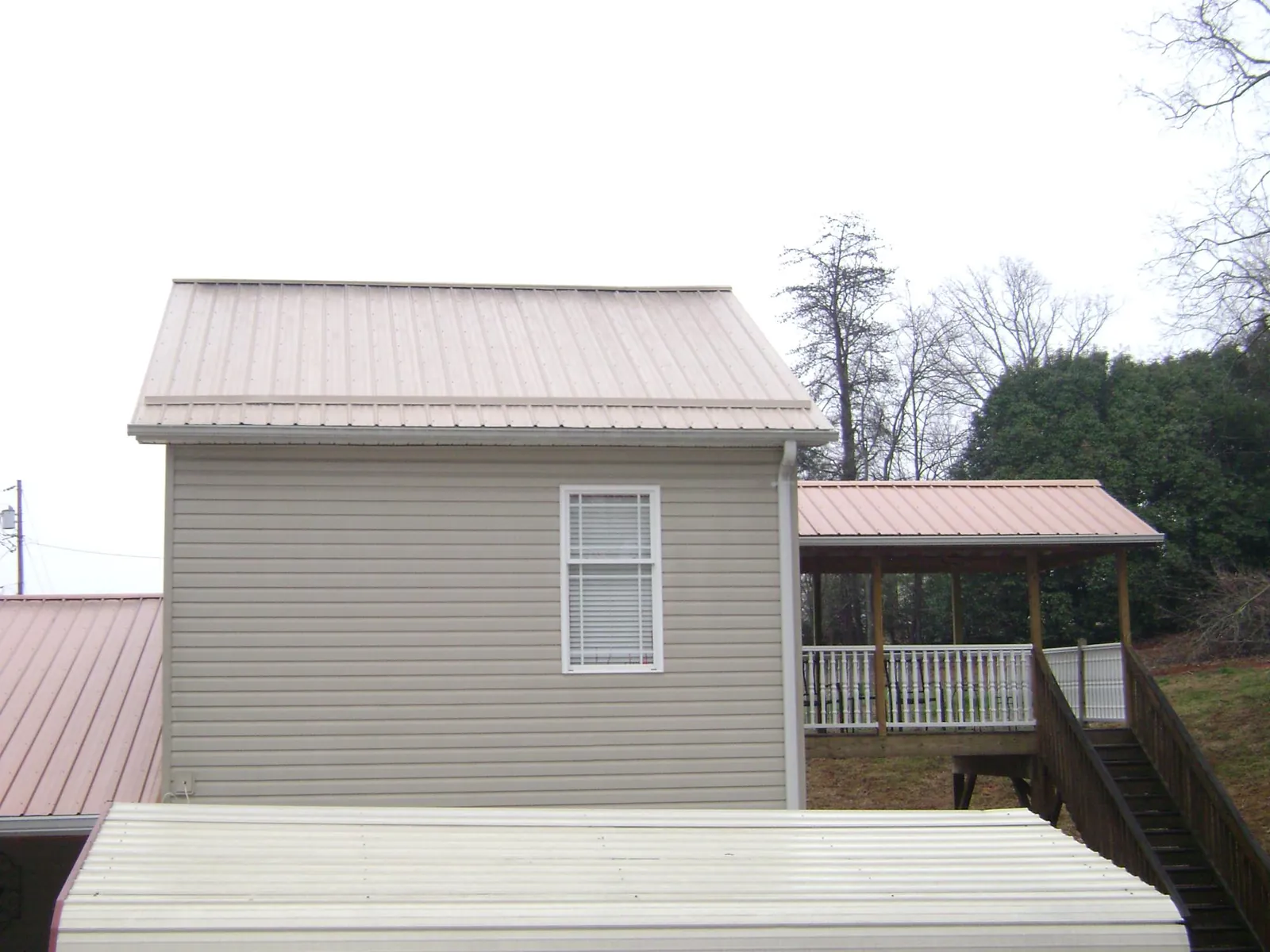Tan metal roofs on a two story addition and attached porch, from a Roof Replacement job in Savage